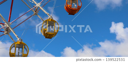Colorful Ferris wheel gondolas against bright blue sky and clouds. Colorful Ferris wheel gondolas against bright blue sky and clouds. 139522531