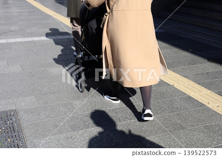 Woman pushing stroller on urban sidewalk Woman pushing stroller on urban sidewalk 139522573