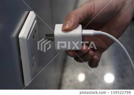 Hand plugging charger into wall socket 139522799
