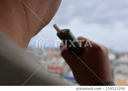 A man smoking an e-cigarette on his balcony. 139523200
