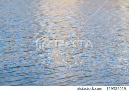 Golden river glow. Shimmering water with warm ripples. Calm river surface reflects serene golden hues. Gentle flowing river displays soft shimmering light and tranquil textures 139524019