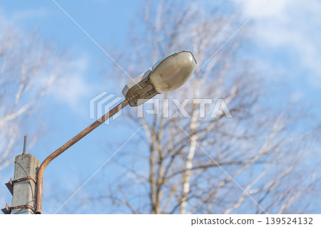 Vintage urban setting featuring aged lamp and leafless trees at sunrise. Rustic street corner showing antique lamp with peeling paint during early morning hours Vintage urban setting featuring aged lamp and leafless trees at sunrise. Rustic street corner showing antique lamp with peeling paint during early morning hours 139524132