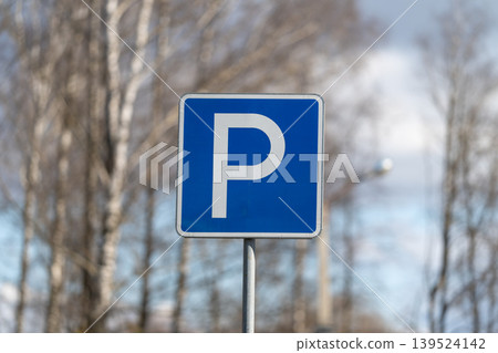 Closeup of parking sign. Bright blue parking sign captured against tree trunks and sky. Photograph showcases blue parking sign with nature elements in minimal style Closeup of parking sign. Bright blue parking sign captured against tree trunks and sky. Photograph showcases blue parking sign with nature elements in minimal style 139524142