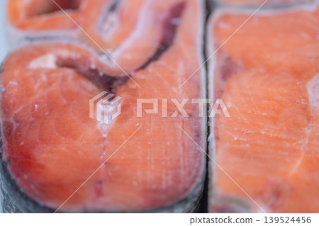 Market display features icy salmon portions. Rustic style with frosted seafood at counter. Handcut frozen salmon pieces showcased at market with rustic display and icy glaze 139524456