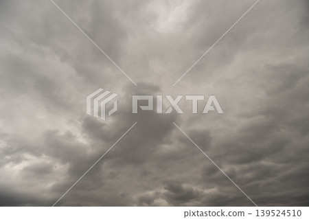 Gray clouds dominate sky atmosphere. Dull sky with thick gray clouds covering completely. Gloomy overcast sky with dense lowhanging clouds creating somber ambiance 139524510