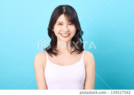 A portrait of a young Japanese woman in a white camisole, smiling against a light blue background. A portrait of a young Japanese woman in a white camisole, smiling against a light blue background. 139527562