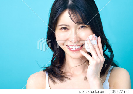 A close-up of a young Japanese woman smiling and holding a powder puff to her cheek. A close-up of a young Japanese woman smiling and holding a powder puff to her cheek. 139527563