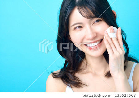 A young Japanese woman looks to the side, shows her teeth, smiles, and places a puff on her cheek. A young Japanese woman looks to the side, shows her teeth, smiles, and places a puff on her cheek. 139527568
