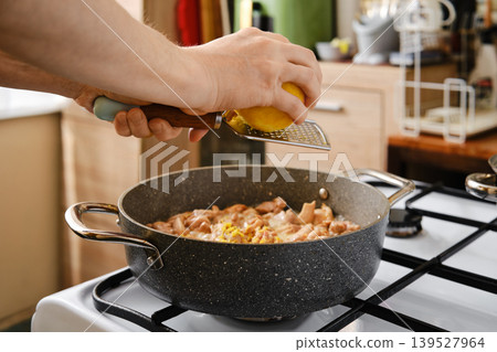 Cooking chicken in a kitchen while grating lemon for flavor Cooking chicken in a kitchen while grating lemon for flavor 139527964