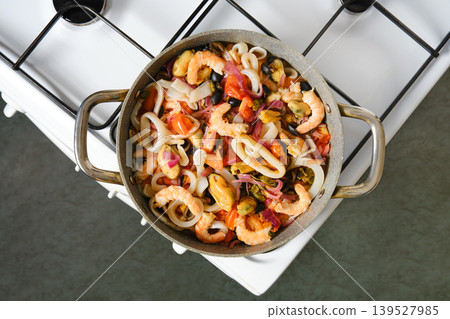 A pot holds a mixture of shrimp, mussels, and squid with chopped tomatoes and onions A pot holds a mixture of shrimp, mussels, and squid with chopped tomatoes and onions 139527985