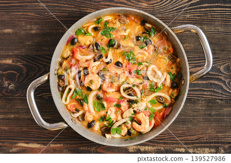 Seafood dish in a pan with mixed ingredients and bright colors served on a wooden table Seafood dish in a pan with mixed ingredients and bright colors served on a wooden table 139527986