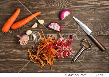 Carrots, garlic, and red onion are prepared on a wooden table with a knife and peeler Carrots, garlic, and red onion are prepared on a wooden table with a knife and peeler 139527995