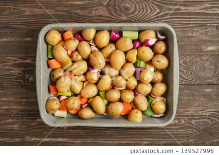 Fresh vegetables and baby potatoes prepared for roasting in a baking dish on a wooden table Fresh vegetables and baby potatoes prepared for roasting in a baking dish on a wooden table 139527998