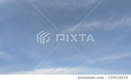 A serene image of a pale blue sky with light, wispy clouds stretching across the frame. The subtle white streaks and patches create a sense of calm and openness. 139528333