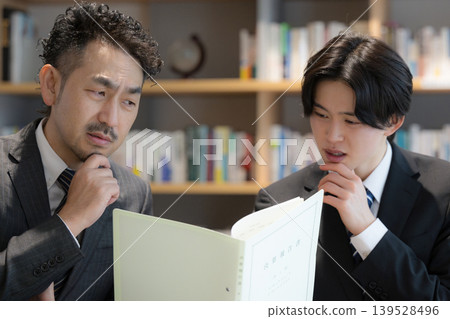 畫面中,一位商人正在書架前與公司總裁商議文件,處理會計師和其他專業人士(例如負責財務報告的人員)的各種問題。 畫面中,一位商人正在書架前與公司總裁商議文件,處理會計師和其他專業人士(例如負責財務報告的人員)的各種問題。 139528496
