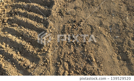 Dry brown soil features rough textures, tractor tire tracks, scattered stones. This natural earth background captures agricultural land under warm sunlight. Perfect for farming, construction themes. Dry brown soil features rough textures, tractor tire tracks, scattered stones. This natural earth background captures agricultural land under warm sunlight. Perfect for farming, construction themes. 139529520