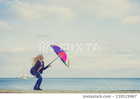 Woman jumping with colorful umbrella on beach Woman jumping with colorful umbrella on beach 139529967