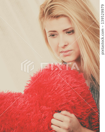 Sad woman holding red pillow in heart shape Sad woman holding red pillow in heart shape 139529979