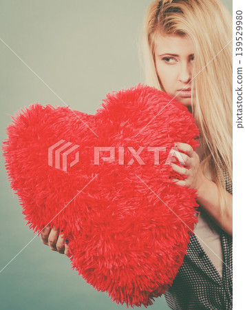 Sad woman holding red pillow in heart shape Sad woman holding red pillow in heart shape 139529980