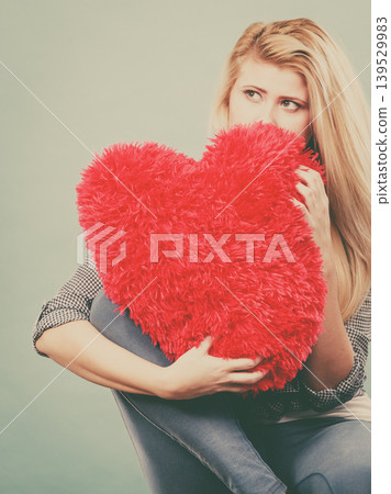 Sad woman holding red pillow in heart shape Sad woman holding red pillow in heart shape 139529983