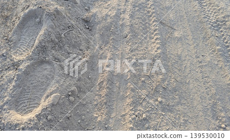 Clear footprints mark dry, sandy soil. This natural ground texture captures rustic earth details, simple outdoor paths. Sunlight illuminates the dusty surface, creating organic patterns. Clear footprints mark dry, sandy soil. This natural ground texture captures rustic earth details, simple outdoor paths. Sunlight illuminates the dusty surface, creating organic patterns. 139530010