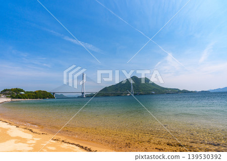 從大三島的沙灘上可以欣賞到瀨戶內海的壯麗景色,俯瞰著多多良橋和生口島,沿著島波海道而行。 從大三島的沙灘上可以欣賞到瀨戶內海的壯麗景色,俯瞰著多多良橋和生口島,沿著島波海道而行。 139530392