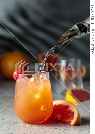 Strong alcohol is poured into a glass with ice and grapefruit juice. Strong alcohol is poured into a glass with ice and grapefruit juice. 139530771