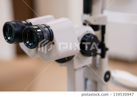Close-up medical device lens for eye examination with black optics on white frame against blurred clinic interior Close-up medical device lens for eye examination with black optics on white frame against blurred clinic interior 139530947