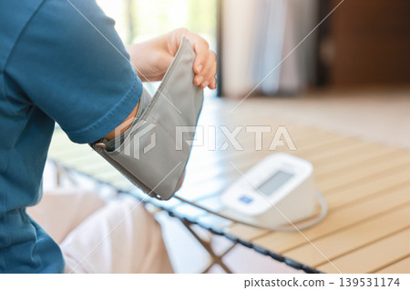 Unrecognizable person putting on blood pressure cuff on arm before measuring with digital monitor at home. Healthcare, cardiology medical concept, monitoring hypertension and daily wellness. Unrecognizable person putting on blood pressure cuff on arm before measuring with digital monitor at home. Healthcare, cardiology medical concept, monitoring hypertension and daily wellness. 139531174