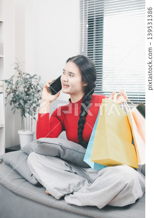 Young Asian woman holding shopping bags and talking on smartphone at home after online shopping, retail purchase, ecommerce order, customer lifestyle and delivery service concept indoors Young Asian woman holding shopping bags and talking on smartphone at home after online shopping, retail purchase, ecommerce order, customer lifestyle and delivery service concept indoors 139531386