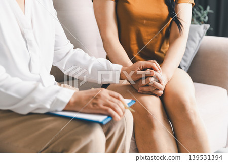 Close up of therapist holding patient hands during mental health counseling session on sofa, conveying empathy, trust, reassurance, emotional support, healing and compassionate care. Close up of therapist holding patient hands during mental health counseling session on sofa, conveying empathy, trust, reassurance, emotional support, healing and compassionate care. 139531394