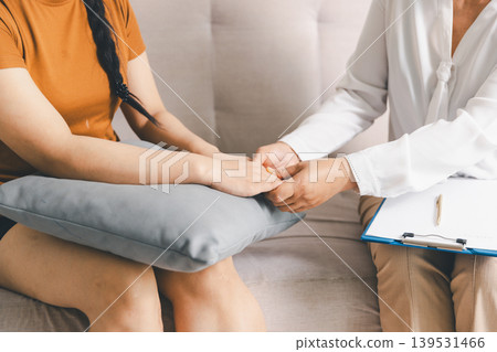 Close up of therapist holding patient hands during mental health counseling session on sofa with pillow for comfort, expressing empathy, trust, reassurance, healing and compassionate care. Close up of therapist holding patient hands during mental health counseling session on sofa with pillow for comfort, expressing empathy, trust, reassurance, healing and compassionate care. 139531466