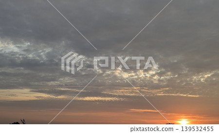 Dark textured clouds fill the dawn sky. The sun glows at the horizon, casting warm orange light. This dramatic atmospheric scene captures natural light transitions, scenic outdoor views at dawn. Dark textured clouds fill the dawn sky. The sun glows at the horizon, casting warm orange light. This dramatic atmospheric scene captures natural light transitions, scenic outdoor views at dawn. 139532455