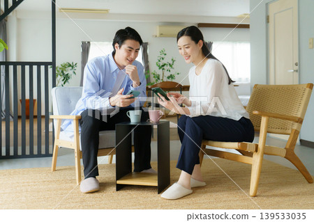 A young Japanese celebrity couple talking on their smartphones in the living room. A young Japanese celebrity couple talking on their smartphones in the living room. 139533035