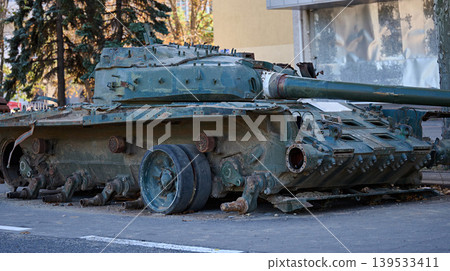 A wrecked Russian tank without tracks on a street in a Ukrainian city, its armor damaged. A wrecked Russian tank without tracks on a street in a Ukrainian city, its armor damaged. 139533411