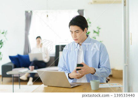A young Japanese man working on his laptop at his table at home. A young Japanese man working on his laptop at his table at home. 139533440