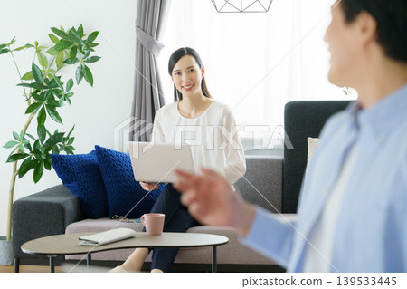 A young Japanese woman talking while using her laptop on a sofa. A young Japanese woman talking while using her laptop on a sofa. 139533445