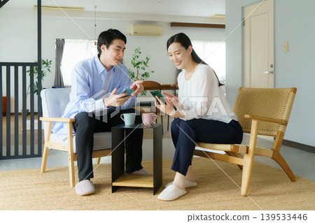 一對年輕的日本明星夫婦在客廳裡用智慧型手機通話。 139533446