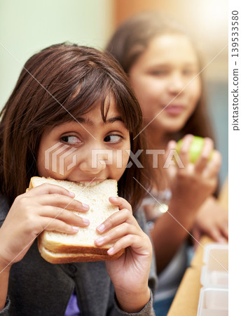 Girl, face and student biting sandwich for meal, break or snack time in classroom at school. Hungry young kid or elementary child eating bread for food, fiber and nutrition in class during recess 139533580