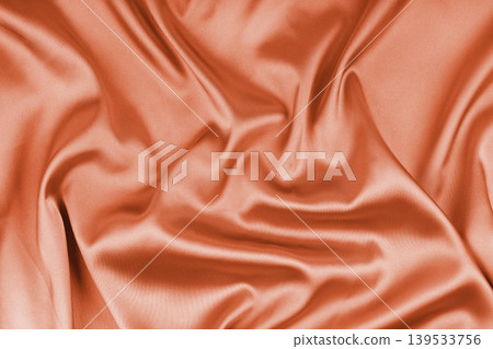 Crumpled, wrinkled orange colored glossy silk satin texture. Shiny smooth fabric with soft folds Crumpled, wrinkled orange colored glossy silk satin texture. Shiny smooth fabric with soft folds 139533756