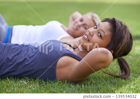 Happy woman, portrait and sit ups for outdoor exercise or workout in fitness together on green grass. Young active female person or people smile for training, health and wellness on field in nature 139534032