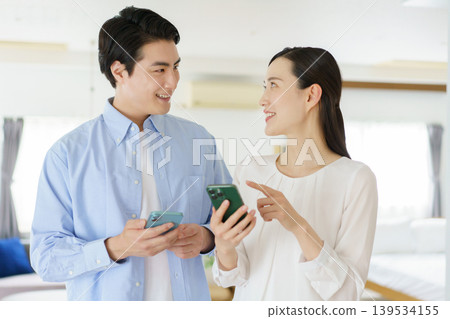 A young Japanese celebrity couple talking on their smartphones in the living room. A young Japanese celebrity couple talking on their smartphones in the living room. 139534155