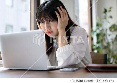 一位日本女性在辦公室裡看著筆記型電腦,陷入沉思。 一位日本女性在辦公室裡看著筆記型電腦,陷入沉思。 139534475