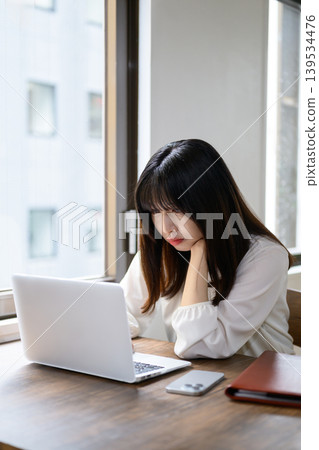 A Japanese woman is looking at her laptop in the office, deep in thought. A Japanese woman is looking at her laptop in the office, deep in thought. 139534476