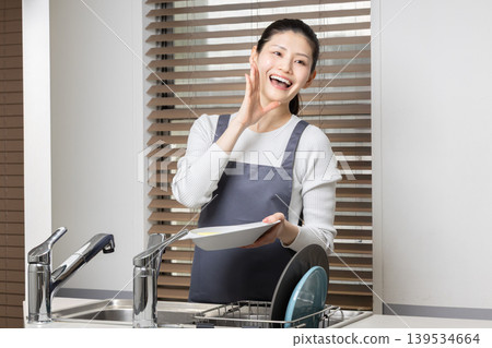 A woman washing dishes with a smile - an image of housework and daily life. A woman washing dishes with a smile - an image of housework and daily life. 139534664