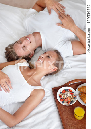 Above of happy couple, morning and breakfast in bed to wake up with food or meal together to relax. Man, smile or woman in home eating healthy snack or drinking juice for diet for love in bedroom Above of happy couple, morning and breakfast in bed to wake up with food or meal together to relax. Man, smile or woman in home eating healthy snack or drinking juice for diet for love in bedroom 139534782