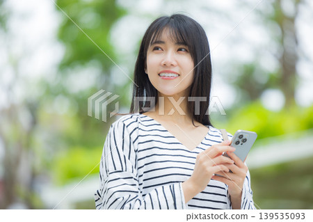 A young woman operating a smartphone outdoors A young woman operating a smartphone outdoors 139535093