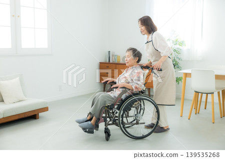一位坐在輪椅上的老年婦女和一位正在照顧她的中年婦女。 一位坐在輪椅上的老年婦女和一位正在照顧她的中年婦女。 139535268