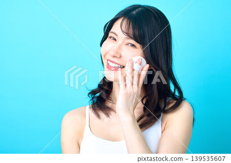 一位年輕的日本女子帶著燦爛笑容，正用粉撲撲上妝。 139535607