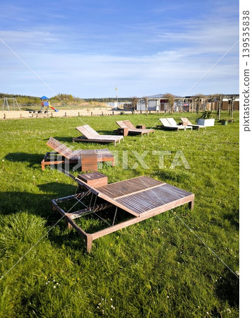 Wooden sun loungers for relaxing on a green lawn under a blue sky. 139535838
